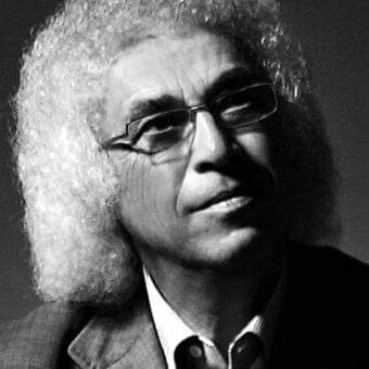 Monochrome portrait of a man with curly hair and glasses looking slightly left with shadowed facial features