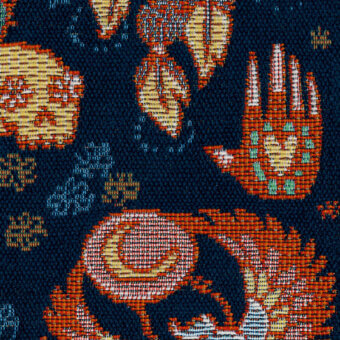 Navy textile with scattered floral and abstract motifs in orange, yellow, teal, and white, featuring a pixelated woven texture.
