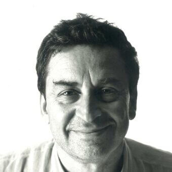 Black and white portrait of middle-aged man, Franco Raggi, with short dark hair, wearing a light collared shirt against a white backdrop.