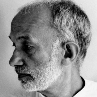 Black and white portrait of Umberto Riva, showing profile view with gray hair, textured beard, and detailed facial features.