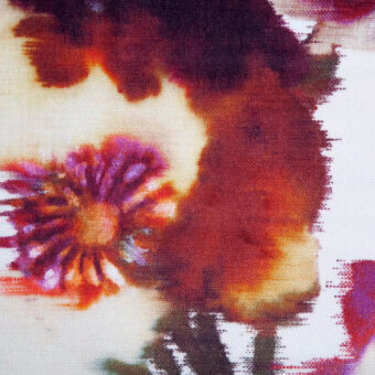 Floral textile pattern with watercolor-style blooms in purple, orange, and brown hues on a white background, showing a granular woven texture.