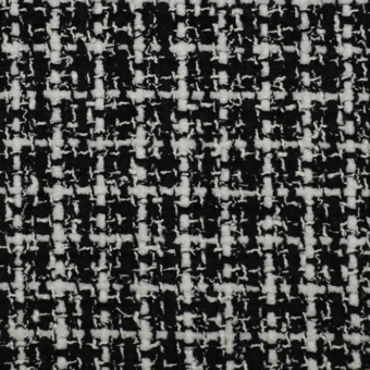 Black and white tweed fabric texture displaying a dense, square pattern from interwoven yarns with a slightly rough, nubby surface.