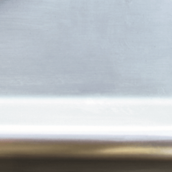 Brushed stainless steel surface with horizontal bands of light gray, white, and bronze tones, displaying a layered composition and diffused lighting.