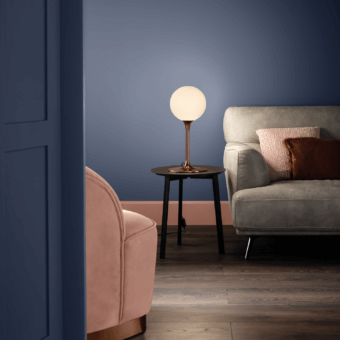 Masiero table lamp, copper finish, white glass shade, placed on a dark wood side table within a modern blue and peach interior.