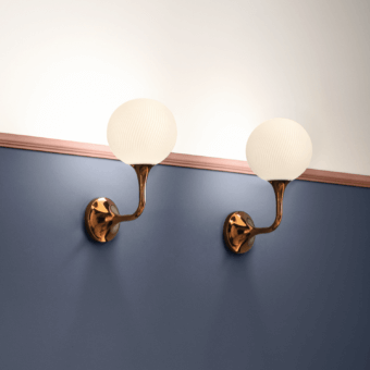 Masiero tee wall lamps, bronze finish, with off-white ribbed glass shades, mounted on a blue and beige wall with copper trim.