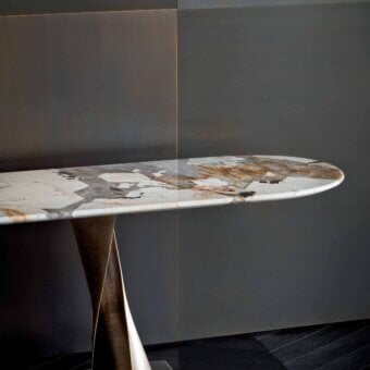 Console table, light stone top with beige, gray, and brown patterns, sculptural dark wood base with metal plinth, gray and bronze wall panels.