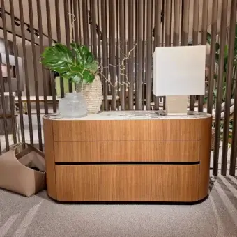 Cassoni dresser, wood and marble, curved two-drawer design with plant and bag, modern interior setting.
