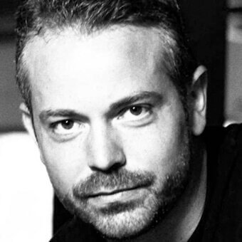 Black and white portrait of Marc Thorpe, showing short dark hair, mustache, beard, angular features, and direct eye contact with soft lighting.