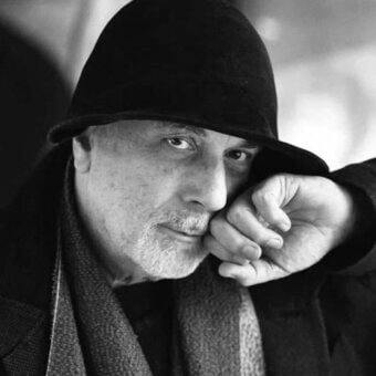 Ron Arad portrait, black and white photography, designer in fedora and scarf, contemplative pose, soft diffused lighting, textured details.