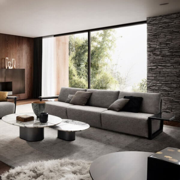 Gray modular sofa with square pillows, white marble coffee tables, dark wood media console, stone accent wall, and shag rug in a modern living room.