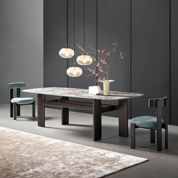 Dining table with gray marble top and dark wood legs, teal chairs, frosted glass pendant lights, pink flowers, dark gray paneled walls.