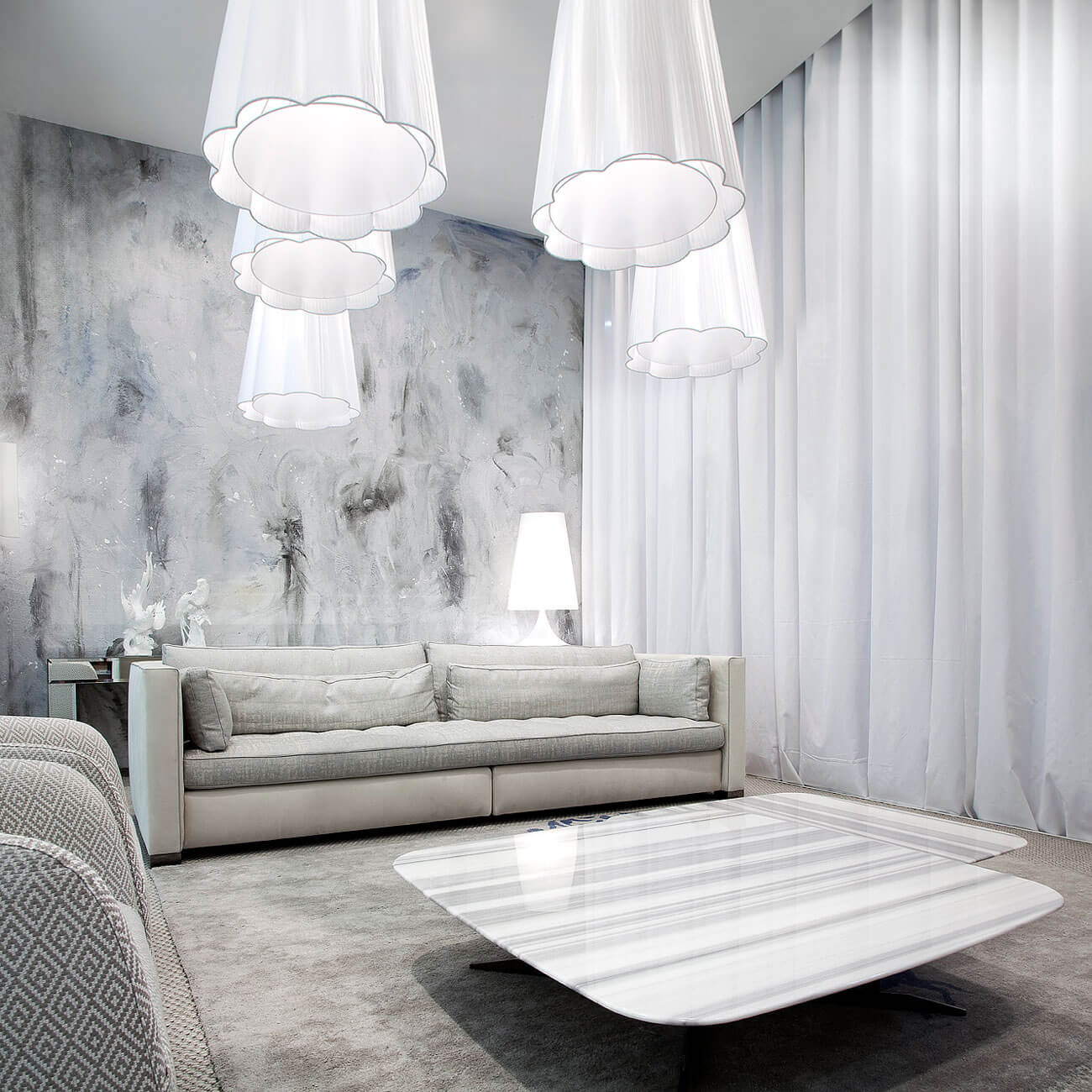 Gray modular sofa with square cushions in a living room featuring white pendant lights, curtains, and a striated coffee table.