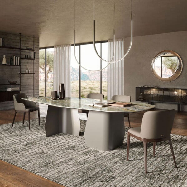 Dining table with green-grey marble top and grey base, surrounded by six light grey chairs, under a circular ring light fixture in a modern dining room.