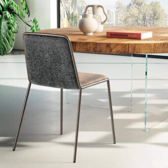 Pletra dining chair, gray textured fabric and tan seat, brushed metal frame with angled legs, styled with table, vase, book, plant.