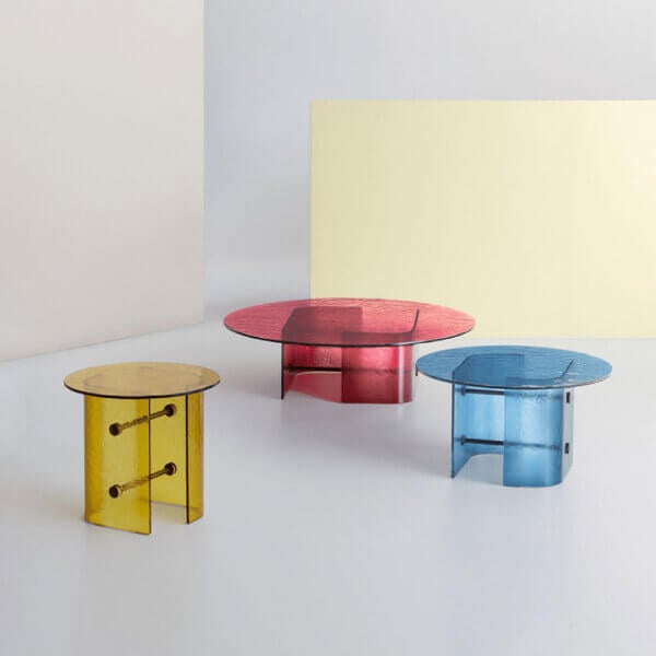 Translucent side tables, yellow, red, and blue, cylindrical base with metal rods, rippled surface, minimalist studio setting.