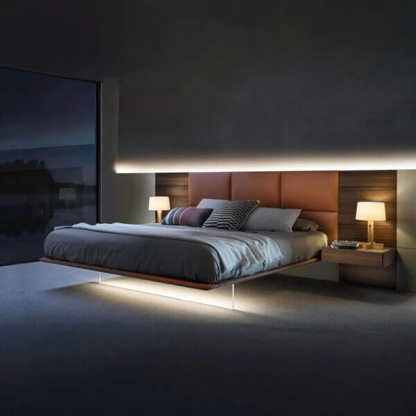 Platform bed with dark wood and gray headboard, terracotta upholstery, white linens, and cylindrical lamps in a contemporary bedroom setting.