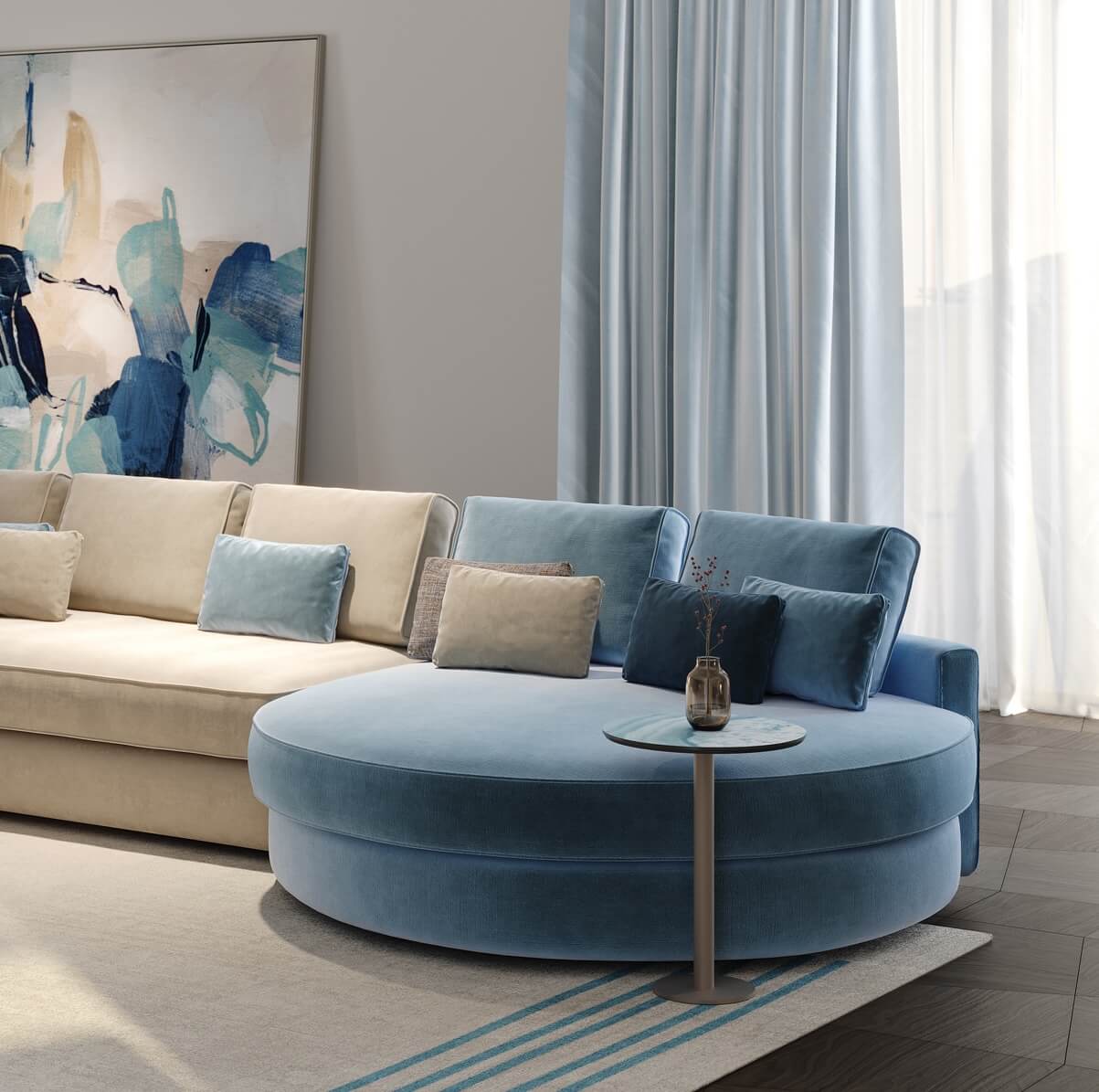 Beige velvet sectional sofa with blue cushions and rounded ottoman, styled with pillows, marble side table, and abstract art.
