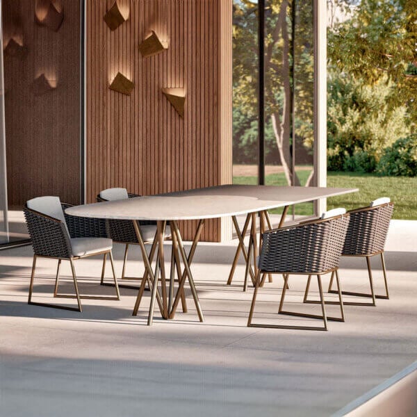 Marble dining table with brass legs and six woven black chairs on a gray tiled patio, modern outdoor setting.