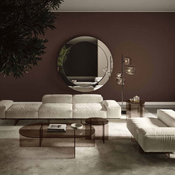 Beige modular sofa with rectangular cushions on gray rug, near mirrored wall, glass coffee tables, floor lamp, and green plant.