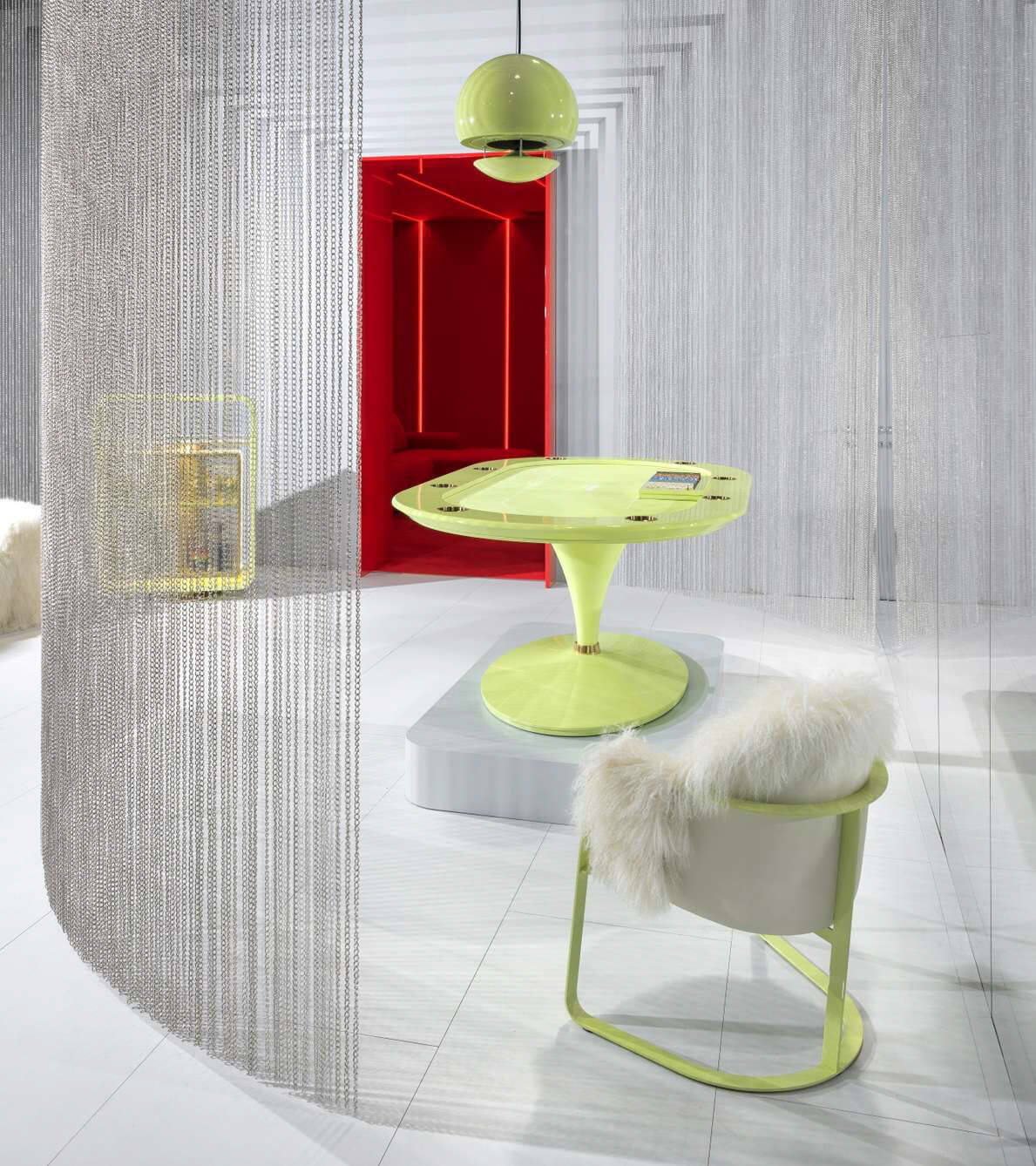 Lime-green table and chair set with rounded table, pedestal base, sheepskin chair, silver chain-link backdrop, white floor.