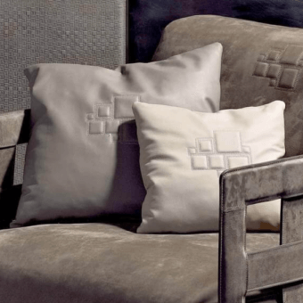 Gray braid cushions on gray velvet armchair, dark metal frame, geometric embroidered squares, soft diffused studio lighting.