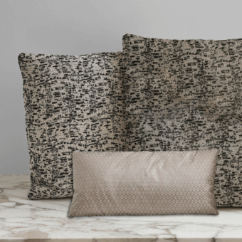 Decorative cushions on white marble: two textured gray cushions, one beige geometric lumbar pillow, soft lighting, neutral background.