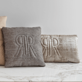 Decorative cushions, gray woven & champagne velvet, embossed monogram, beige diamond pattern, tan leather, on white marble surface.