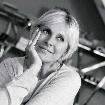 Black and white portrait of Elena Viganò with platinum blonde bob, silver ring, and dangling earrings in a studio setting.