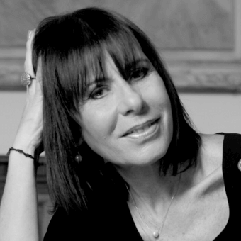 Black and white portrait of a woman with dark hair, silver necklace, ornate ring, and relaxed expression against a blurred interior background.