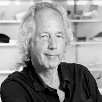 Man portrait, gray hair, dark shirt, slight smile, blurred office background, “heiliger” text, soft lighting, skin texture visible.