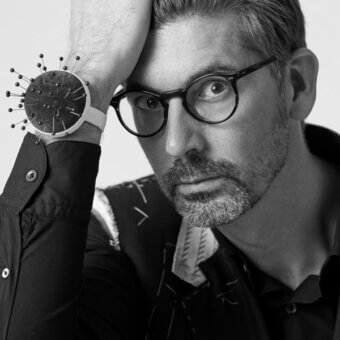 Portrait of José Manuel Ferrero wearing a patterned jacket and wristwatch with metallic pins, against a white background.