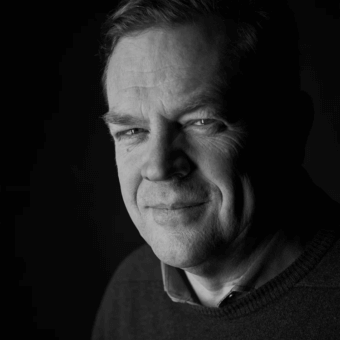 Black and white portrait of a man with short hair, wearing a dark sweater, gazing right with contemplative expression and dramatic lighting.