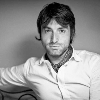 Black and white portrait of Lorenzo Remedi, wearing a white shirt and dark patterned undershirt, with neutral expression and direct gaze.