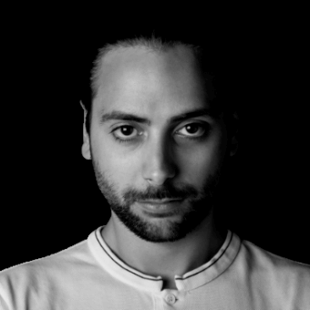 Black and white portrait of Martino Batto, dark hair, short beard, neutral expression, light collared shirt, focused gaze, even lighting.