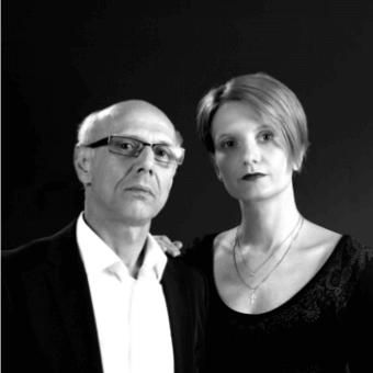 Black and white portrait of Norberto Delfinetti and Monica Bernasconi, dark attire, formal pose, grayscale palette, indistinct background.