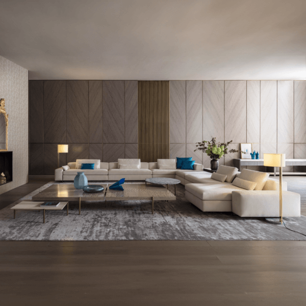 Beige modular sofa with blue pillows on gray rug in living room with chevron wood paneling, brass tables, and ceramic decor.
