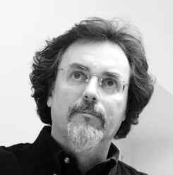 Black and white portrait of Paolo Salvadè, a man with graying dark wavy hair, a full beard, and rectangular glasses, wearing a dark collared shirt.