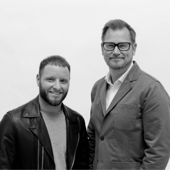 Black and white portrait of two smiling men, s. tollgard & f. castellani, wearing jackets and blazers against a white backdrop.
