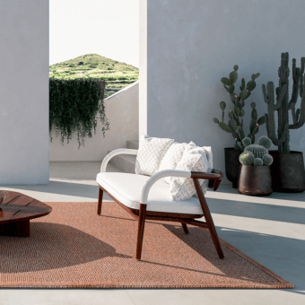 Jiselle sofa, dark wood frame, woven rope detail, cream textured cushions, terracotta rug, cacti, outdoor setting.