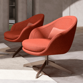 Lucille lounge chairs, reddish-orange fabric, rounded cocoon shape, brushed metal five-star base, coral pillow, modern interior setting.