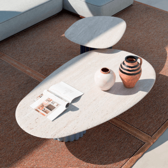 Pablito coffee table, beige stone top, oval shape, with cream fluted base, styled with magazines and ceramic vases on woven rug.