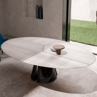 Circular talos table, light gray wood tabletop with linear grain, dark gray sculptural base, and cylindrical stool on tiled floor.