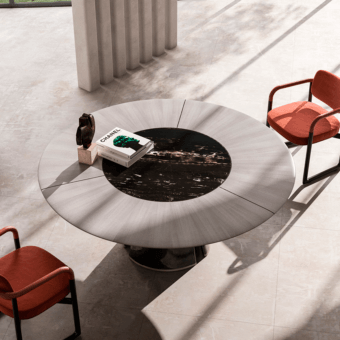 Round dining table with wood veneer and marble inlay, brushed silver base, paired with reddish-brown fabric armchairs, modern minimalist style.