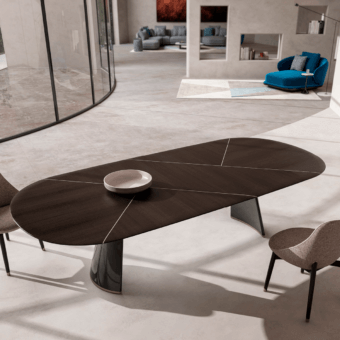 Dark brown talos table, wood and geometric panels, with black pedestal base, in minimalist gray interior with chairs and fireplace.