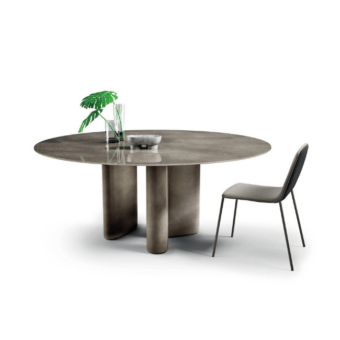Round Lago hoa table, dark gray matte finish, with cylindrical legs and monstera leaf, beside a gray dining chair.