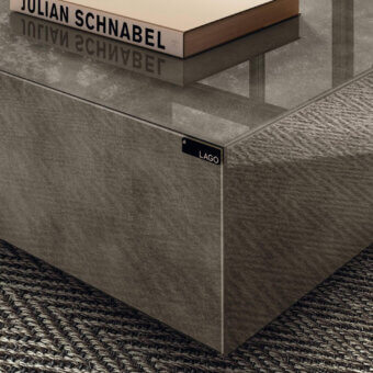 Lago materia coffee table, gray textured surface, stepped panel base, rectangular shape, glossy sheen, dark gray rug, book stack.