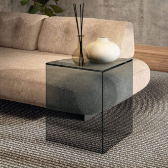 Lago snip coffee table, smoked grey glass top, cube shape, dark grey textured base, modern living room setting, beige sofa backdrop.
