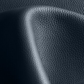 Dark blue pebbled leather texture with a diagonal fold, displaying a fine-grained, matte finish and subtle tonal variations under diffused lighting.