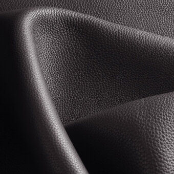 Black leather texture, folded swatch with pebble grain, displaying a curved edge and subtle tonal variations against a dark backdrop.