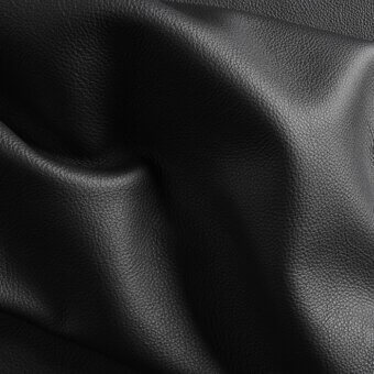 Black leather sheet with textured, granular surface and matte finish, displaying folded curves and shadows in diffused studio lighting.